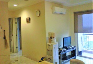 A living room with a television, a clock, and a window. - Adaru Property @city Home Apartmen KLP GDG by Zuzu (Jakarta)