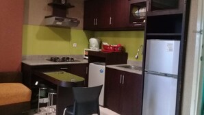 A compact kitchen with a gas stove, a refrigerator, a sink, and a small countertop. There are two chairs and a bench. - Adaru Property @city Home Apartmen KLP GDG by Zuzu (Jakarta)