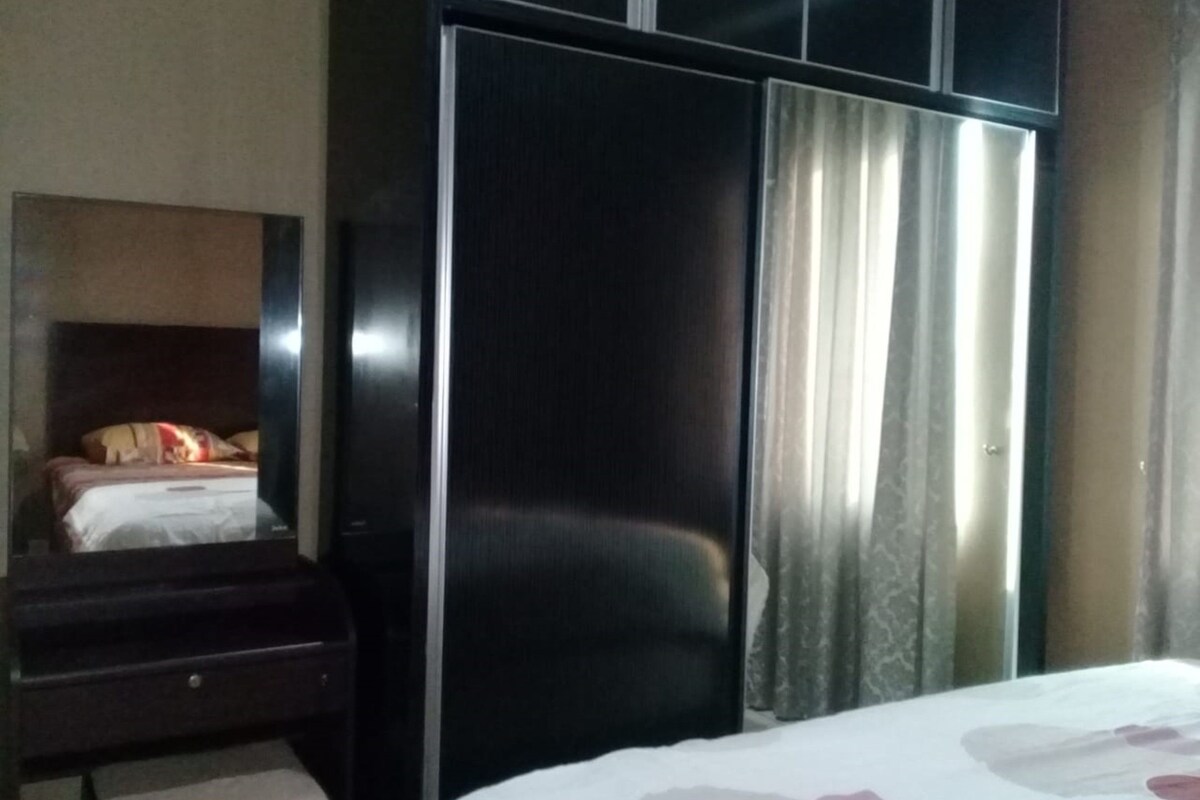 A hotel room with a bed, a wardrobe, a mirror, and a window with curtains.