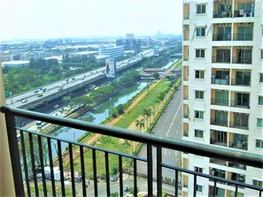 A high-rise building with multiple floors, a view of a busy highway with vehicles, and a river running parallel to the road. - Adaru Property @city Home Apartmen KLP GDG by Zuzu (Jakarta)
