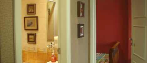 A bathroom with a toilet, sink, and mirror. There are framed pictures on the wall and a red door.