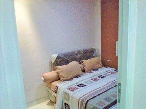 A small, narrow room with a bed against the wall, a door on the right, and a white wall. - Adaru Property @city Home Apartmen KLP GDG by Zuzu (Jakarta)