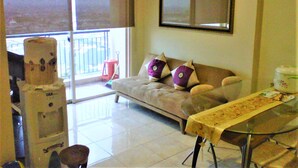 A living room with a sofa, a glass table, and a window with blinds. - Adaru Property @city Home Apartmen KLP GDG by Zuzu (Jakarta)
