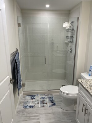 Un baño moderno con cabina de ducha de vidrio, inodoro y lavabo con encimera de granito.