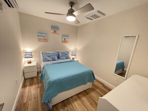 Un dormitorio con cama, dos mesitas de noche, un ventilador de techo y decoración en la pared.