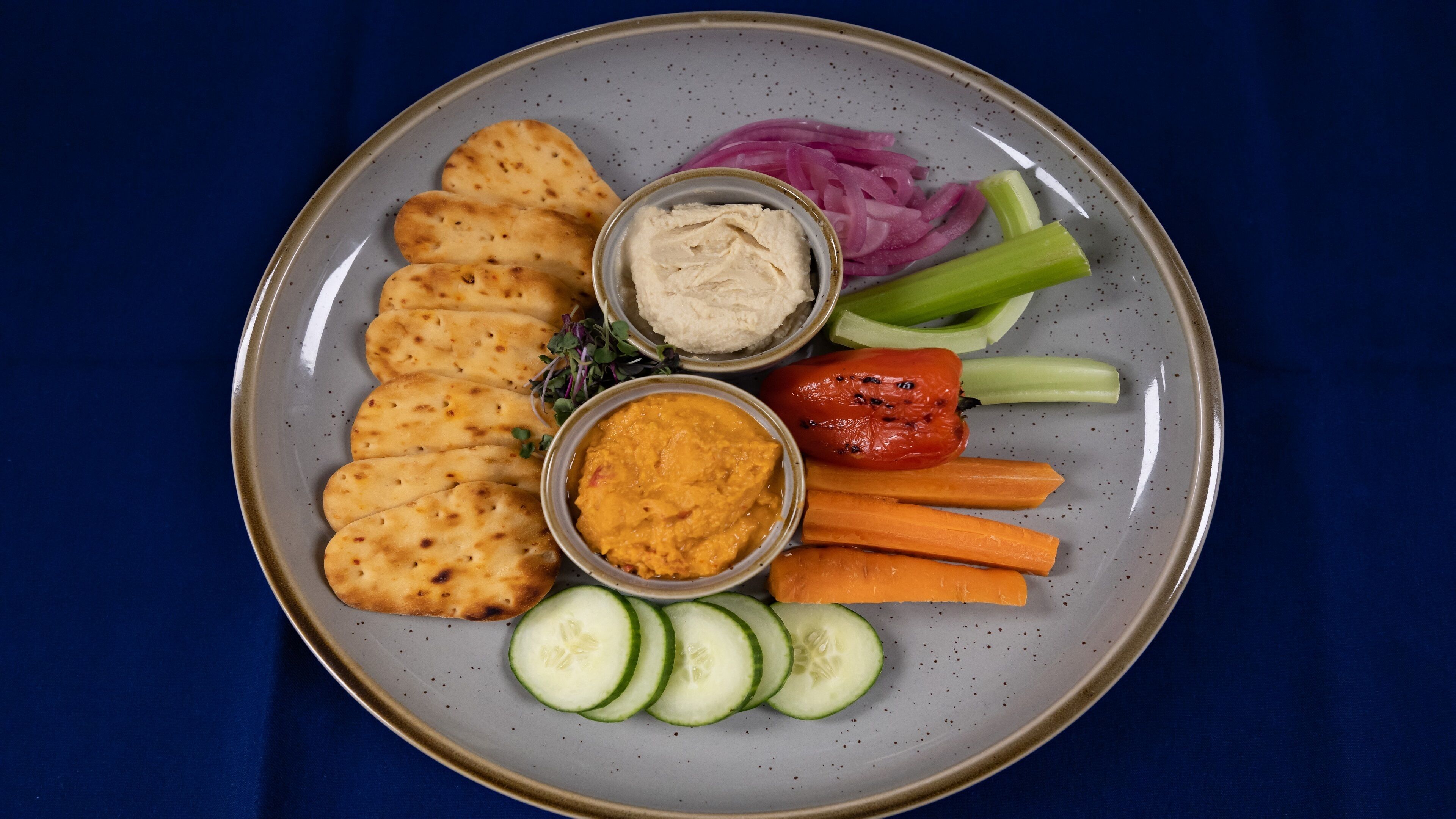 En tallrik med tunnbröd, hummus, morötter, gurka, selleri, röd lök och en röd paprika.