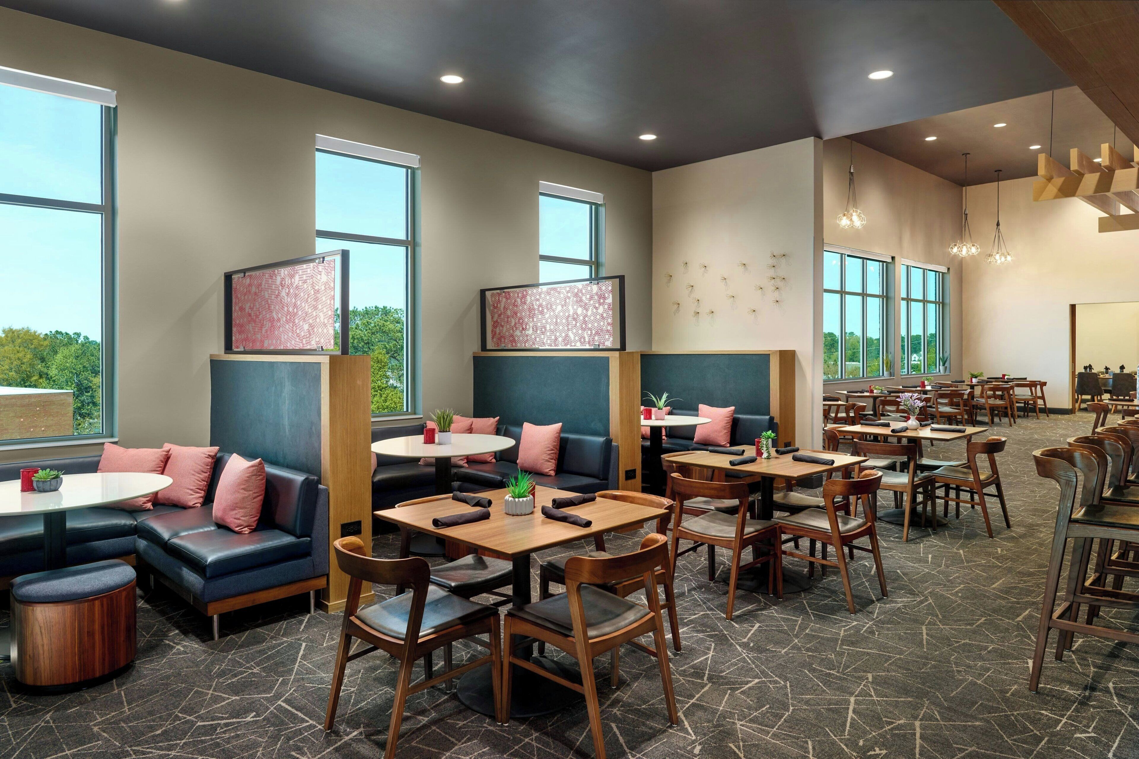 A modern restaurant with high tables and booths, large windows, and a stone-patterned floor.