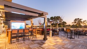 An outdoor patio with wooden flooring, bar seating, and a large screen. - Courtyard® by Marriott® Atlanta Dunwoody (Atlanta)