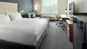 A hotel room with a large bed, a desk with a chair, a television, and a window with a view of the outdoors.