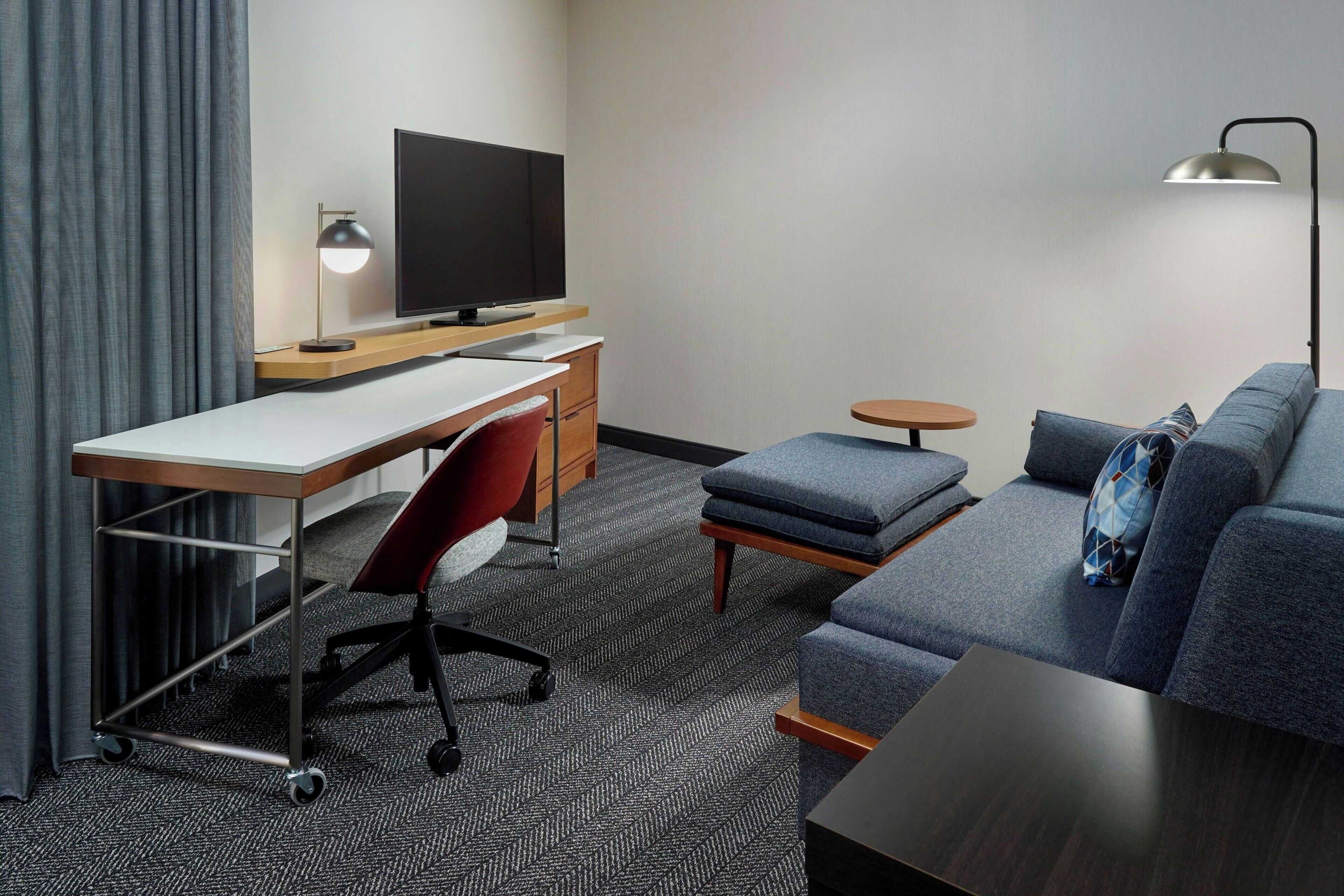 A hotel room with a desk, a television, a sofa, and a lamp.