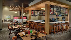 A restaurant with multiple dining tables and chairs, a bar area with a counter, and a kitchen in the background. - Courtyard® by Marriott® Atlanta Dunwoody (Atlanta)