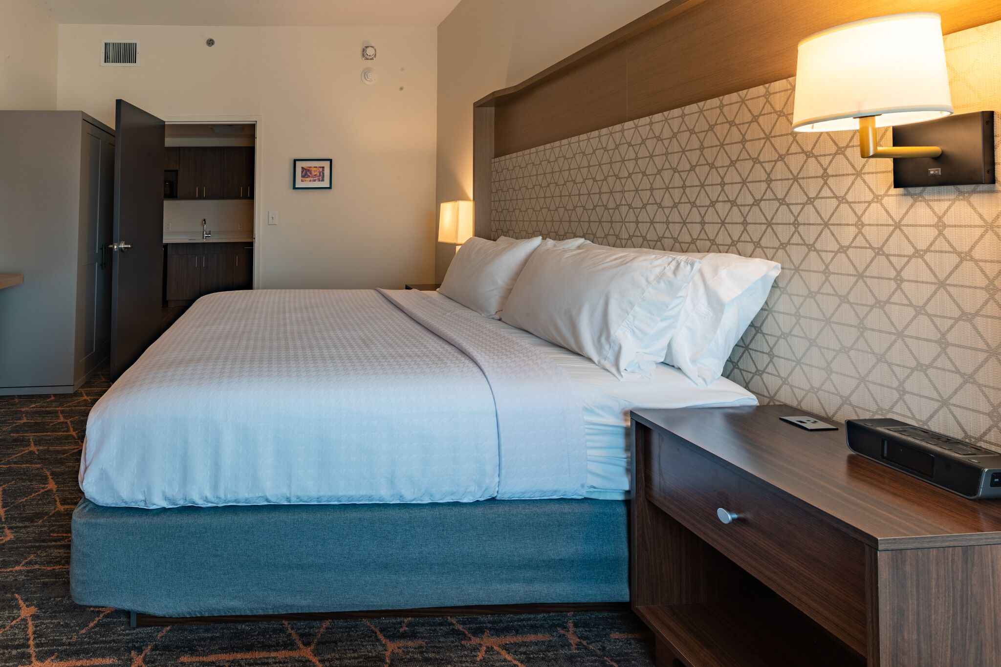 A hotel room with a bed, bedside table, lamp, and a wardrobe.