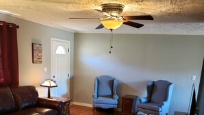 Una sala de estar con ventilador de techo, dos sillones, un sofá, una mesa de centro y un televisor.
