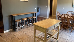 Una cocina con una barra de madera y taburetes, una mesa de comedor con sillas y un cartel enmarcado en la pared.