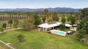 Une grande maison avec une piscine, entourée d’une pelouse bien entretenue et d’arbres.