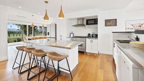 Une cuisine moderne dotée d’un grand îlot central, de tabourets de bar, d’appareils électroménagers en acier inoxydable et de luminaires suspendus.