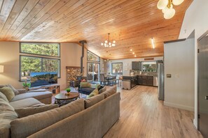 A spacious living area with a large sofa, a dining table, and a kitchen in the background. - Modern upgraded Tahoe Donner 3BR mountain cabin! Pet friendly! (Truckee)