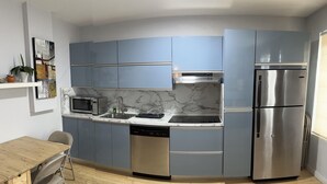 Eine kompakte Küche mit blauen Schränken, einem Edelstahl-Kühlschrank, einer Mikrowelle und einem Geschirrspüler.