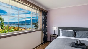 A hotel room with a large window offering a scenic view of mountains and a body of water.