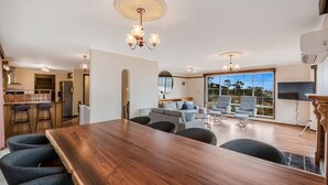 A spacious living area with a large wooden dining table, comfortable seating, and a large window offering a view of the outdoors.