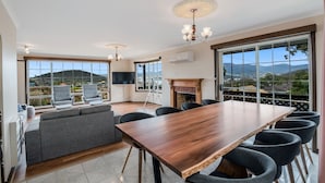 A spacious room with a large wooden table, comfortable seating, a fireplace, and large windows offering a scenic view.