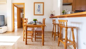 A dining area with a wooden table and chairs, a kitchen in the background, and a framed artwork on the wall. - Roquemar by Interhome (L'Ampolla)