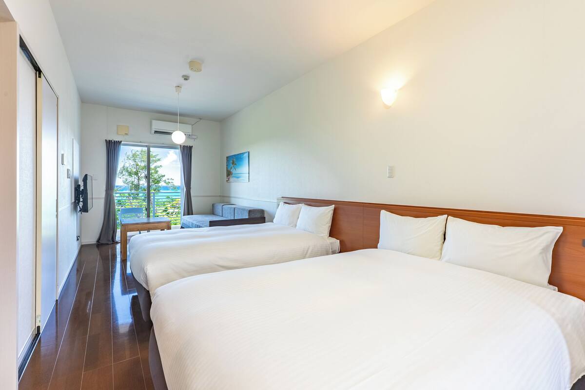A hotel room with three beds, a wooden headboard, a small table, and a view of the outdoors.