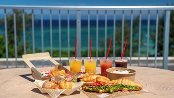 Un tavolo con cibo e bevande su un balcone con vista sull'oceano.