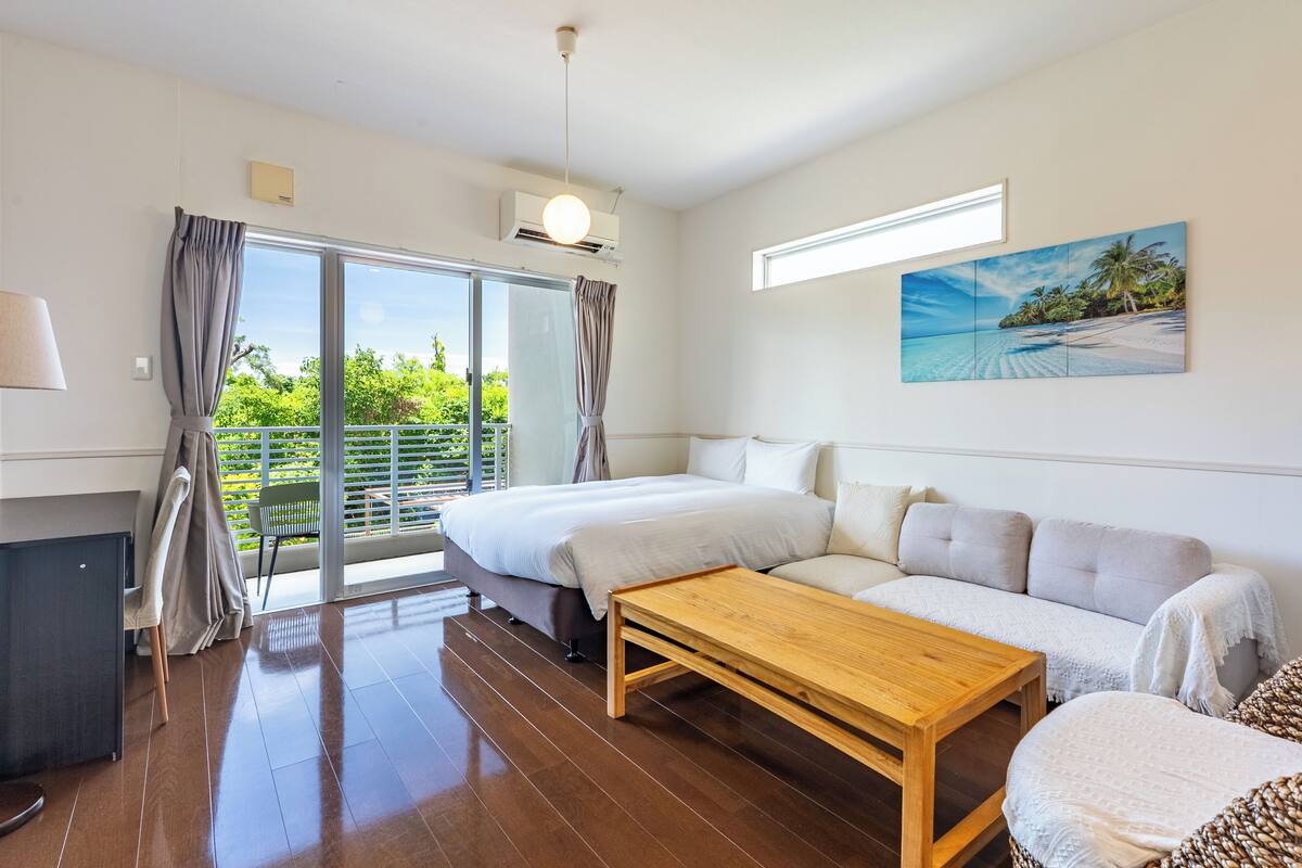 A modern hotel room with a bed, sofa, wooden coffee table, and a painting of a beach scene.