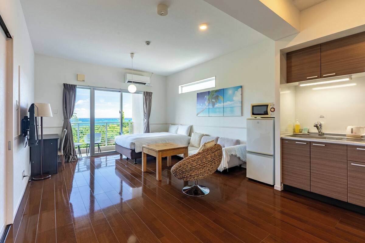 A modern hotel room with a balcony, a dining area, and a kitchenette.