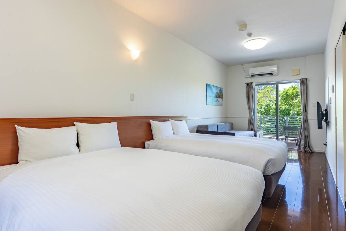 A hotel room with two large beds, a wooden headboard, a small desk, and a window with curtains.