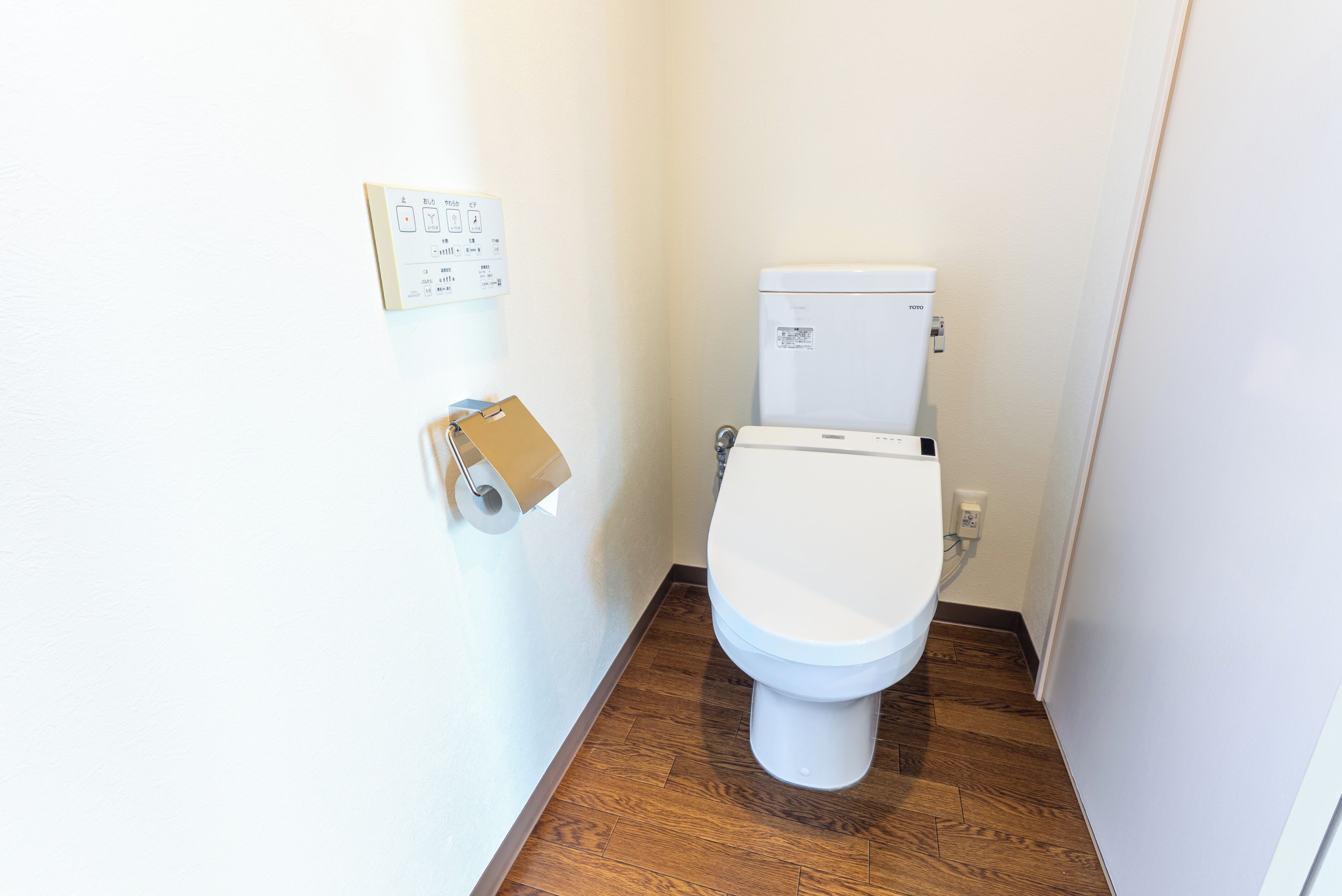 A small, clean bathroom with a toilet, a toilet paper holder, and a wall-mounted electrical outlet.