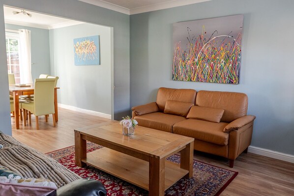 A living room with a brown leather sofa, a wooden coffee table, and a colorful abstract painting on the wall.