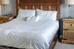 A neatly made bed with white linens, a wooden headboard, and bedside tables with lamps and clocks.