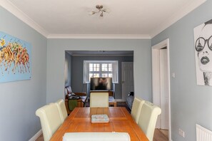 A dining area with a wooden table, white chairs, and a television.