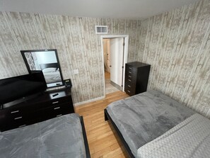 Une chambre avec deux lits, une commode, un miroir et une porte donnant sur une autre pièce.