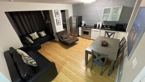 Ein modernes Wohnzimmer mit einer schwarzen Couch, einem Esstisch mit Stühlen, einer Küchenzeile inklusive Geräte und einer Wand mit Muster.