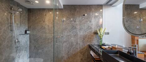 Un baño moderno con ducha envuelta en vidrio, lavamanos de mármol oscuro y un espejo grande.