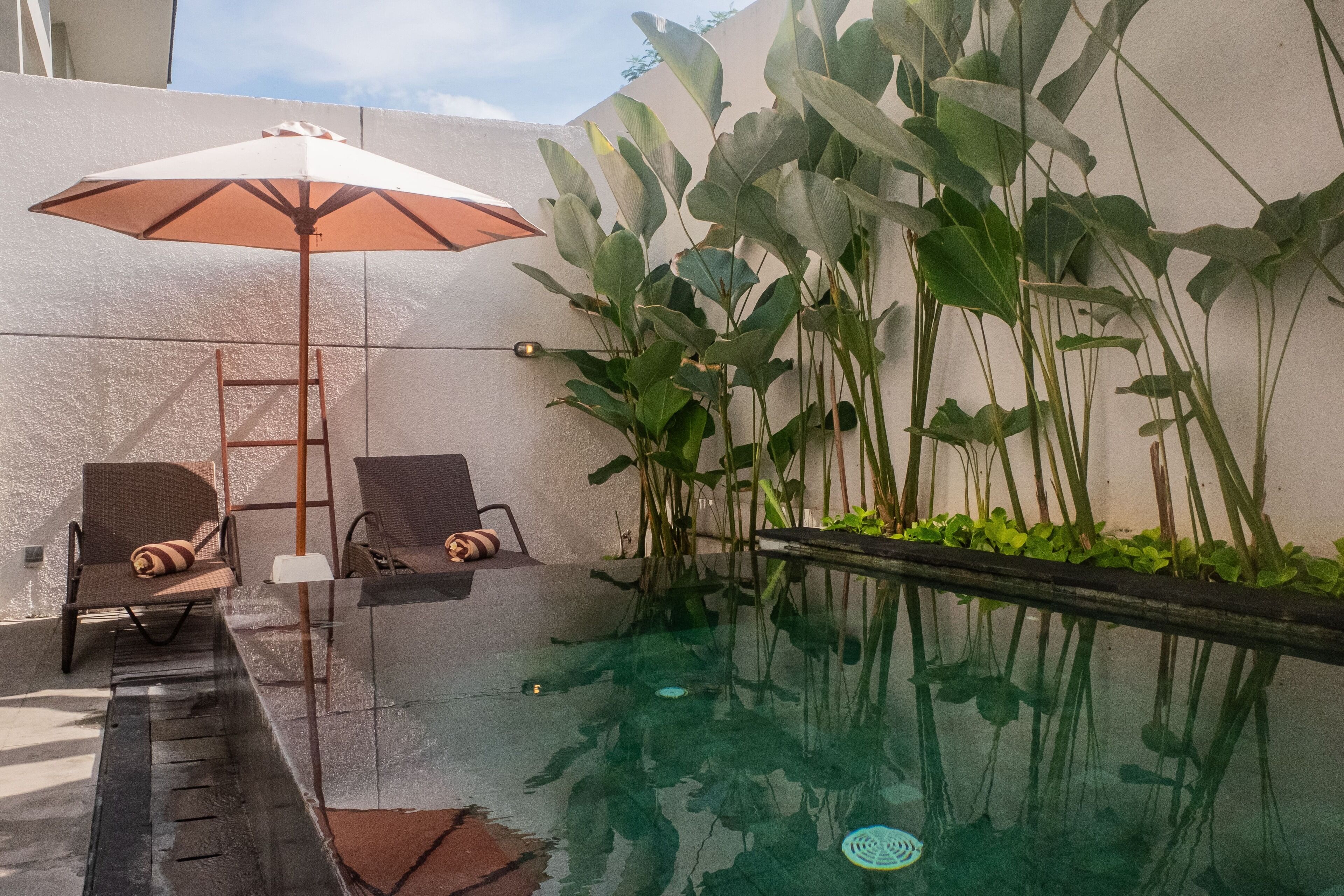 Piscina interna com água cristalina, rodeada por cadeiras de lounge e um guarda-sol.