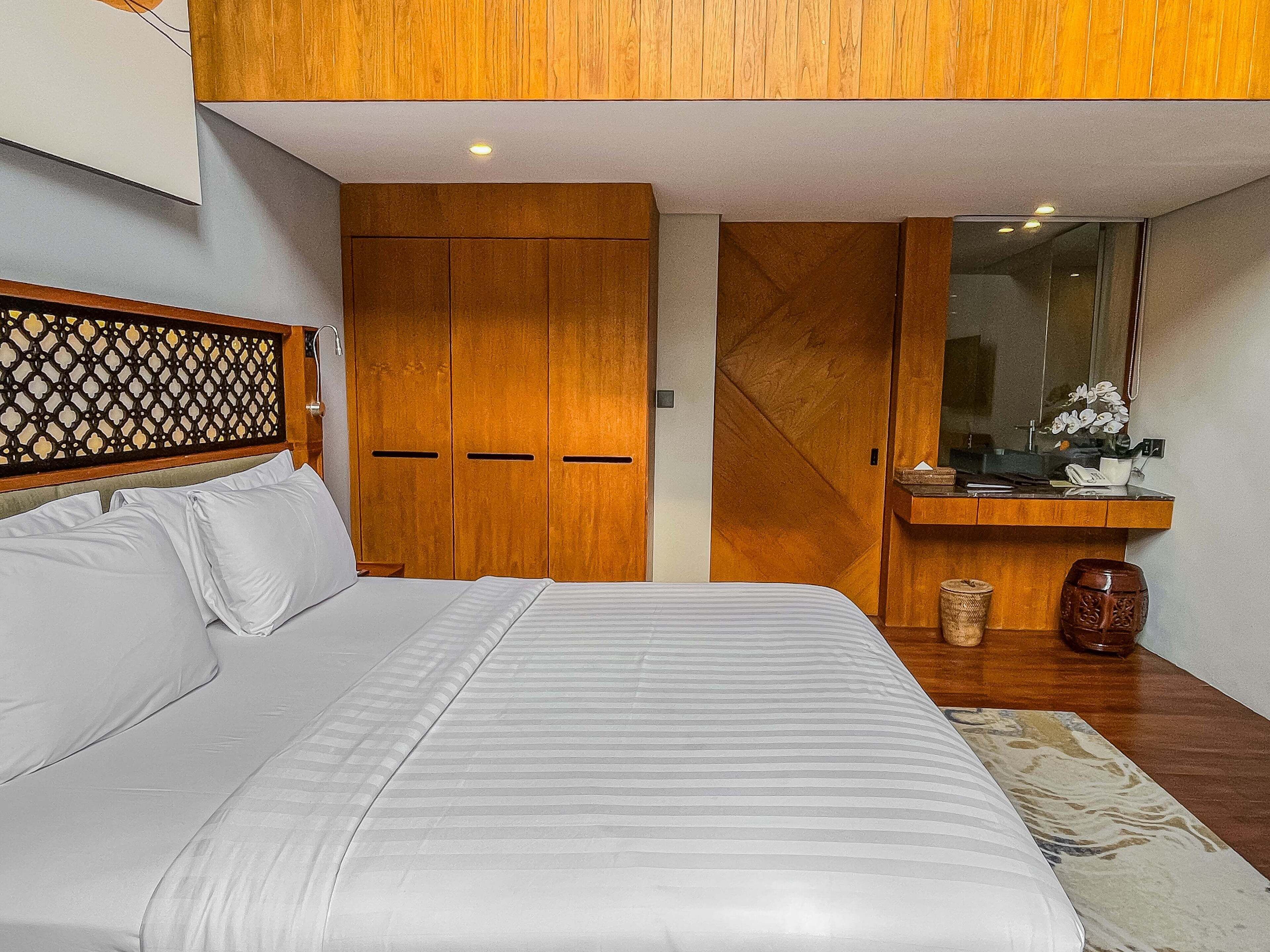 A bedroom with a bed, wooden wardrobe, and a small desk with a mirror.