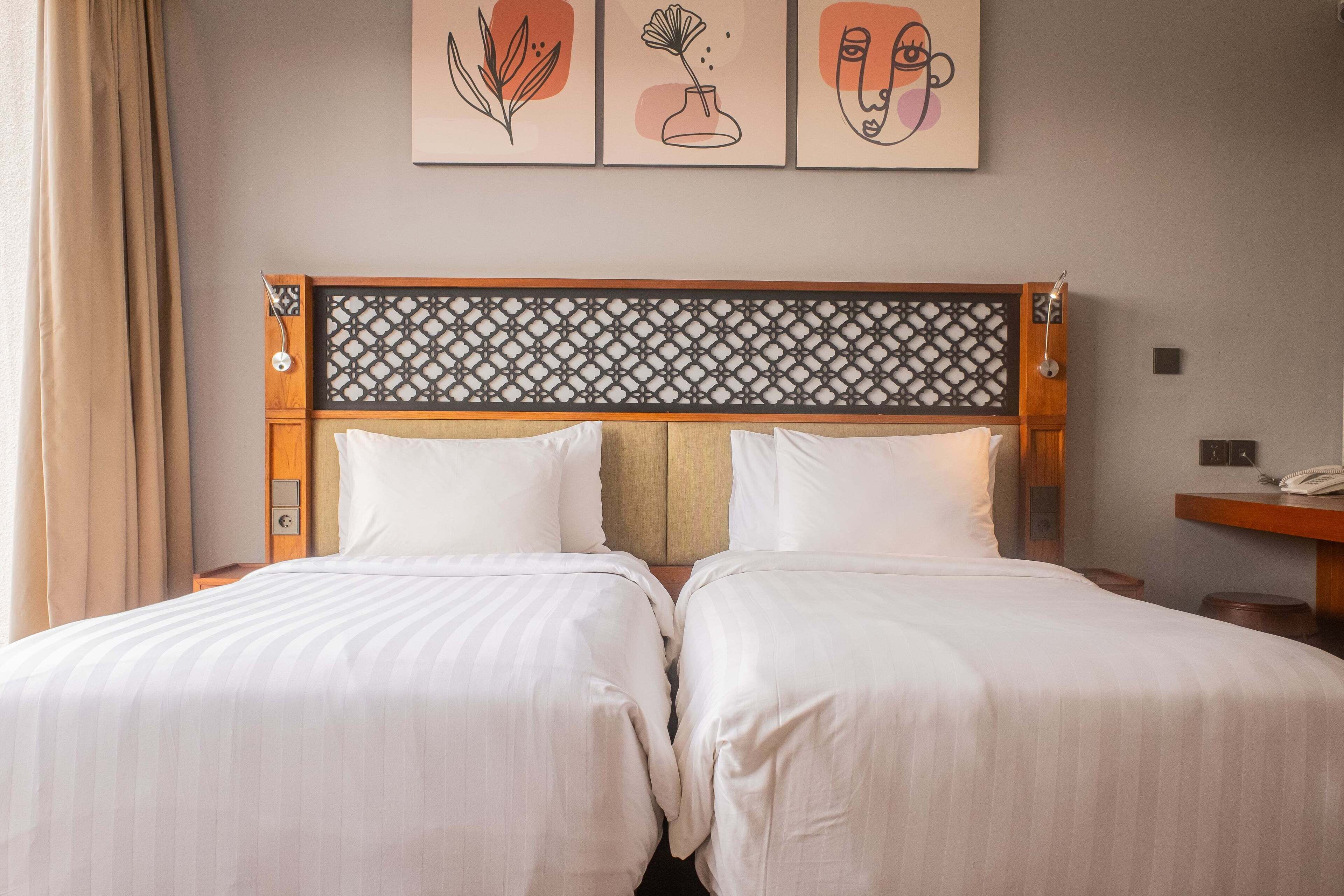 Cama de casal com cabeceira estampada, duas mesas de cabeceira e telefone fixado na parede.