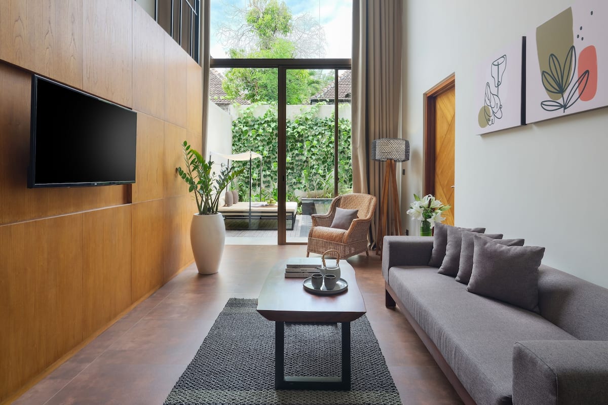 A modern living room with a flat-screen TV, a sofa, a coffee table, and a wicker chair.