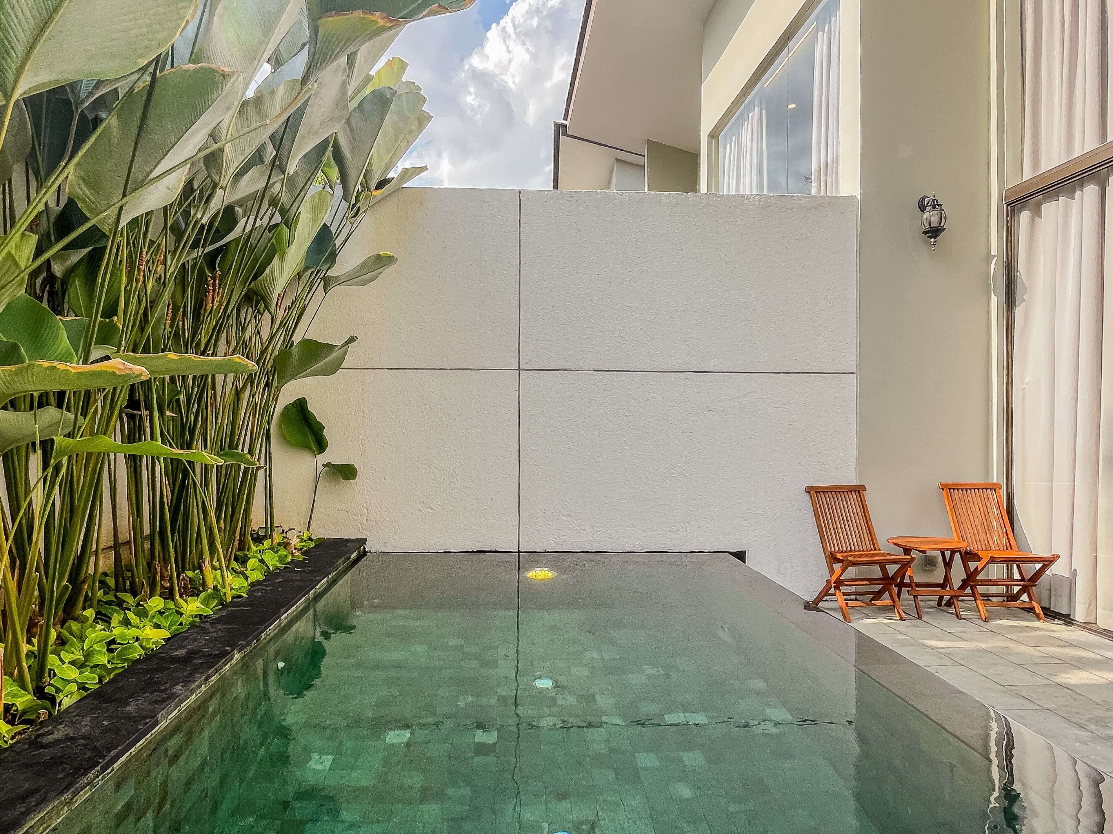 A modern outdoor pool area with a tiled floor, surrounded by lush greenery and wooden chairs.