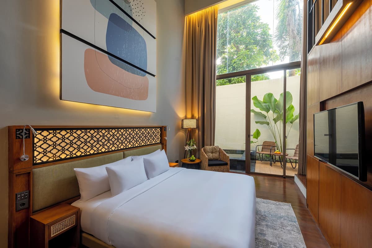 A modern hotel room with a large bed, a TV, a small table with a lamp, and a view of the outdoors.