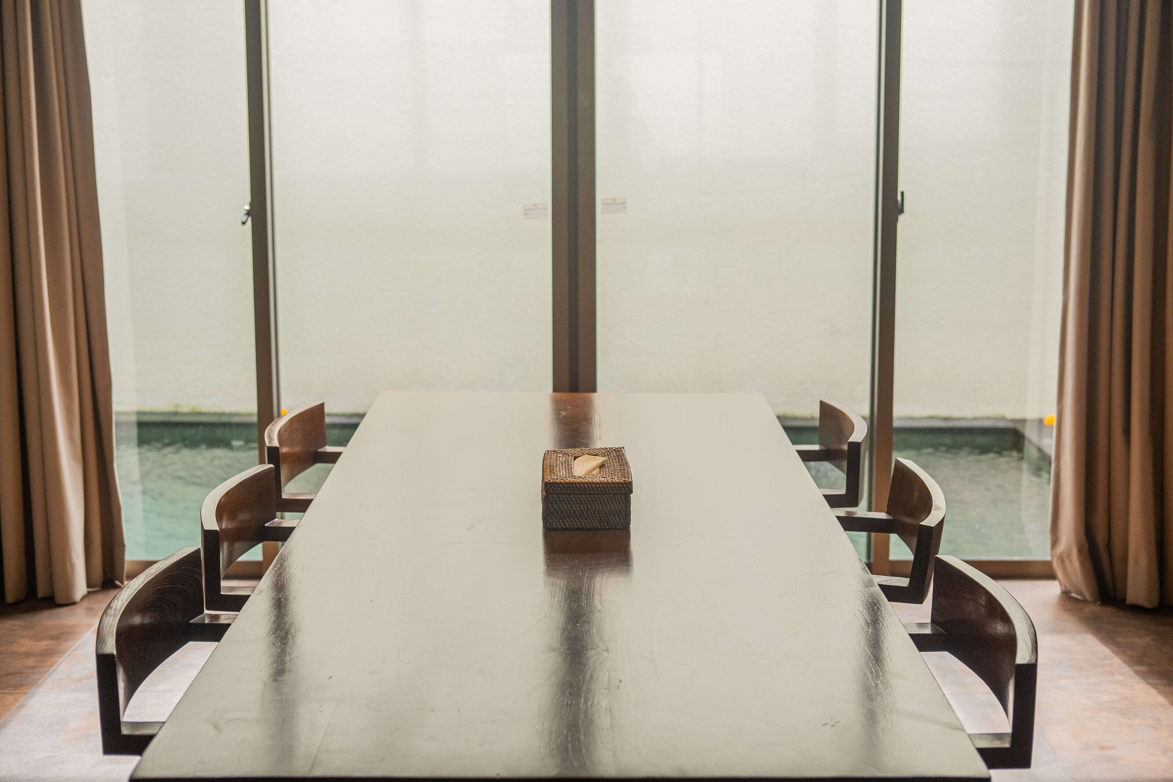 A long table with chairs, a small box, and a view of water through large windows.