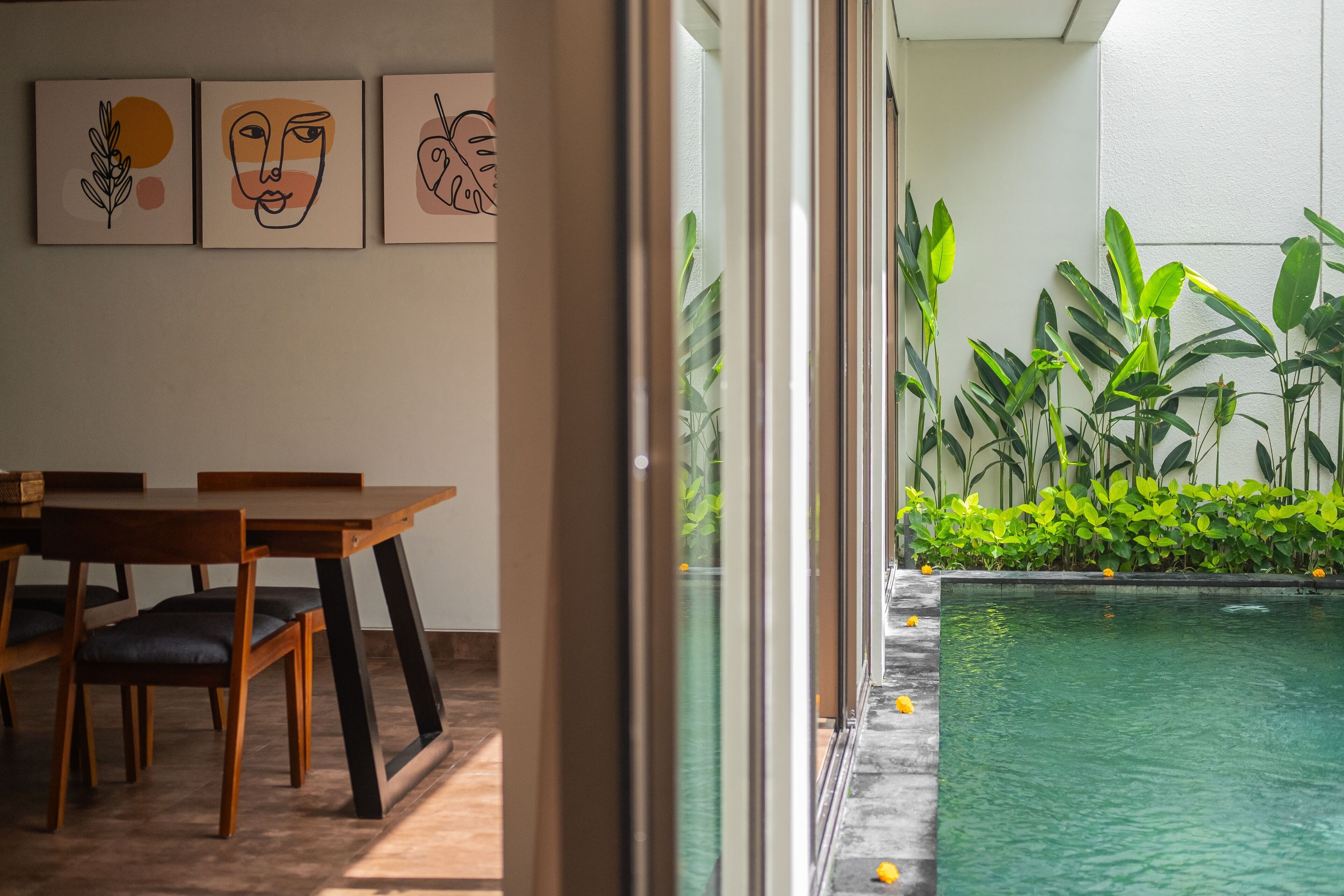 A modern interior with a dining area, a pool, and lush greenery.