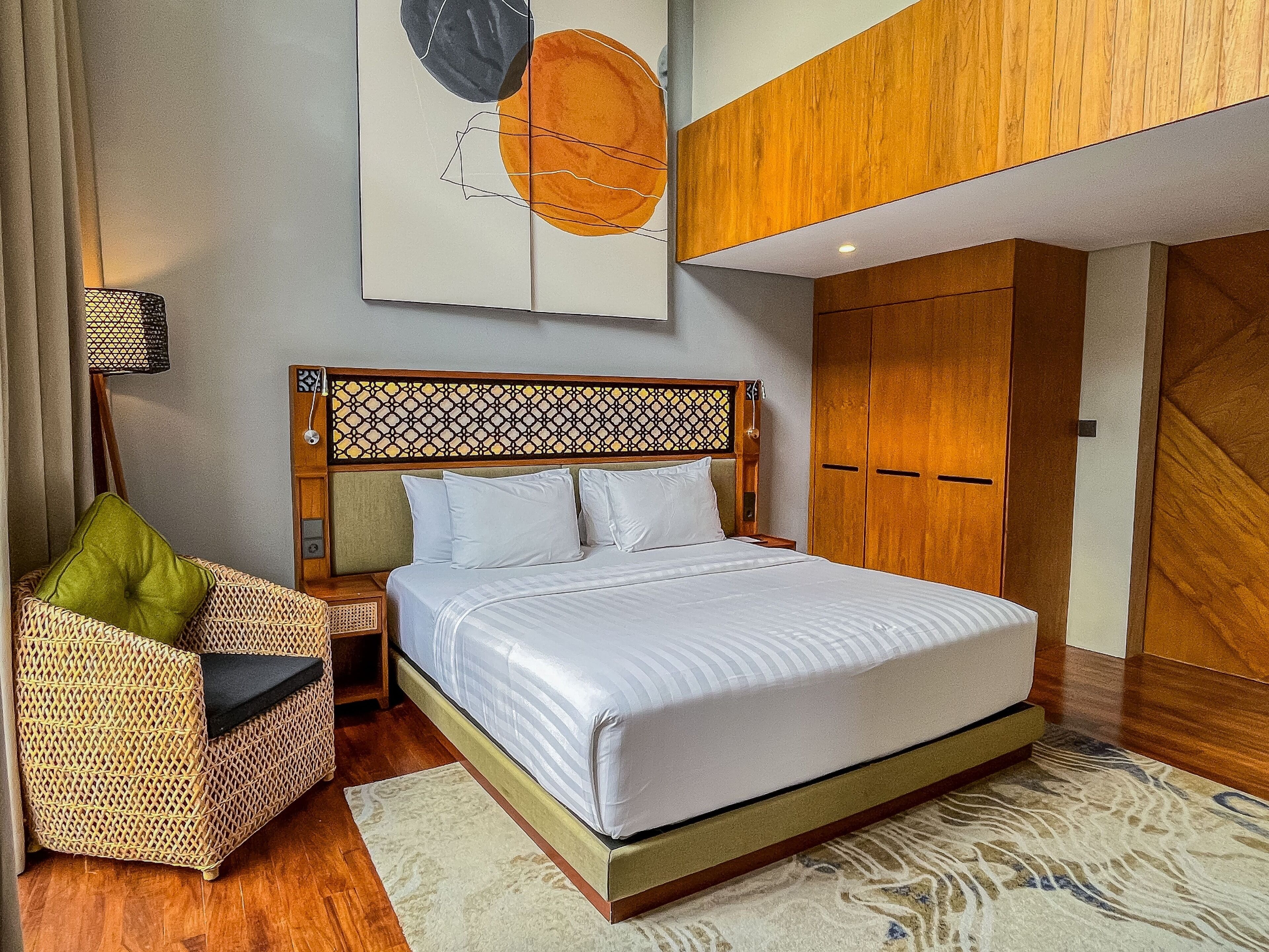 A neatly arranged bedroom with a bed, a wicker chair, a lamp, and a wardrobe.
