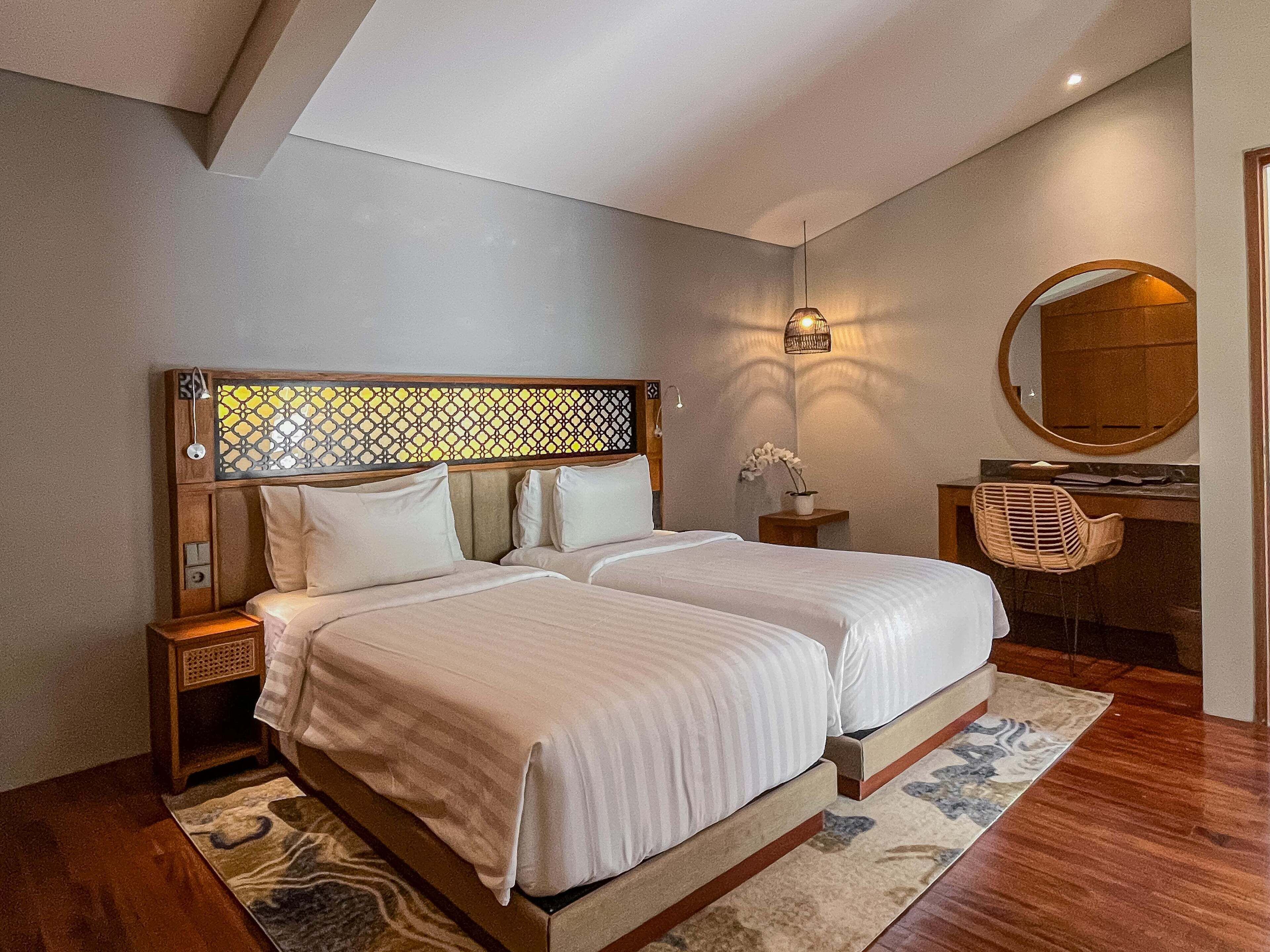 A double bed with a wooden headboard, bedside tables, a desk with a chair, a mirror, and a small potted plant.