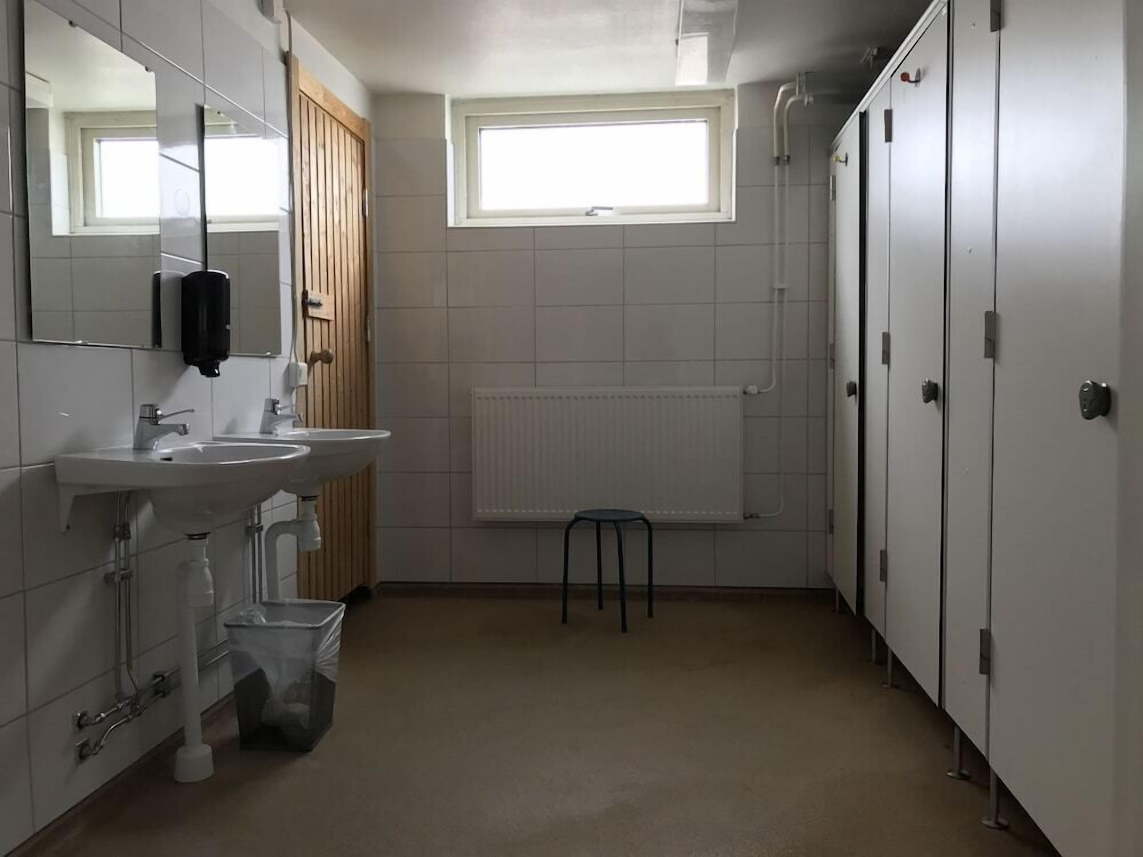 Ett badrum med handfat, spegel och toalett. Det finns ett fönster som släpper in naturligt ljus och ett element för uppvärmning.
