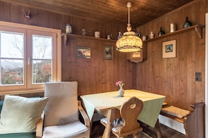 Une pièce aux murs lambrés, avec une table à manger, des chaises, un vase rempli de fleurs et une lampe suspendue.